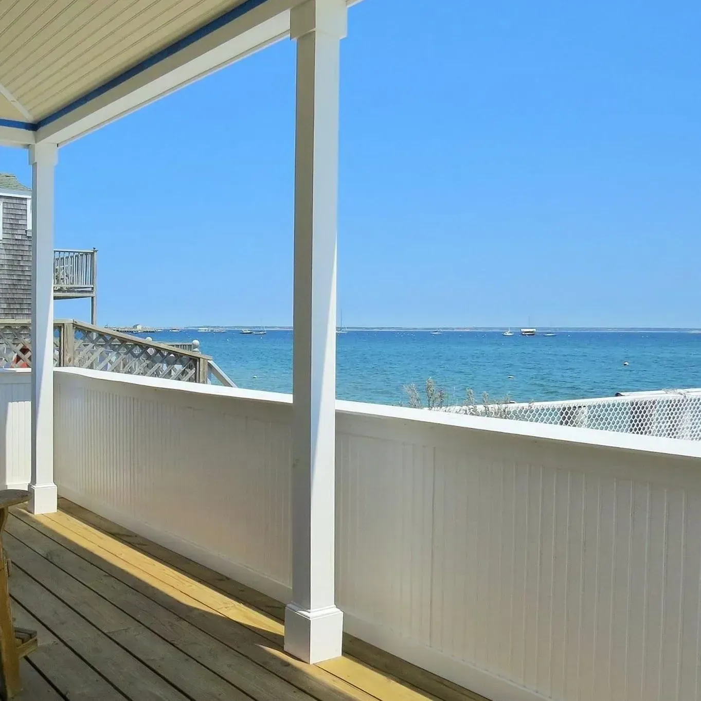 Wooden porch with white railing overlooks blue ocean and sky.