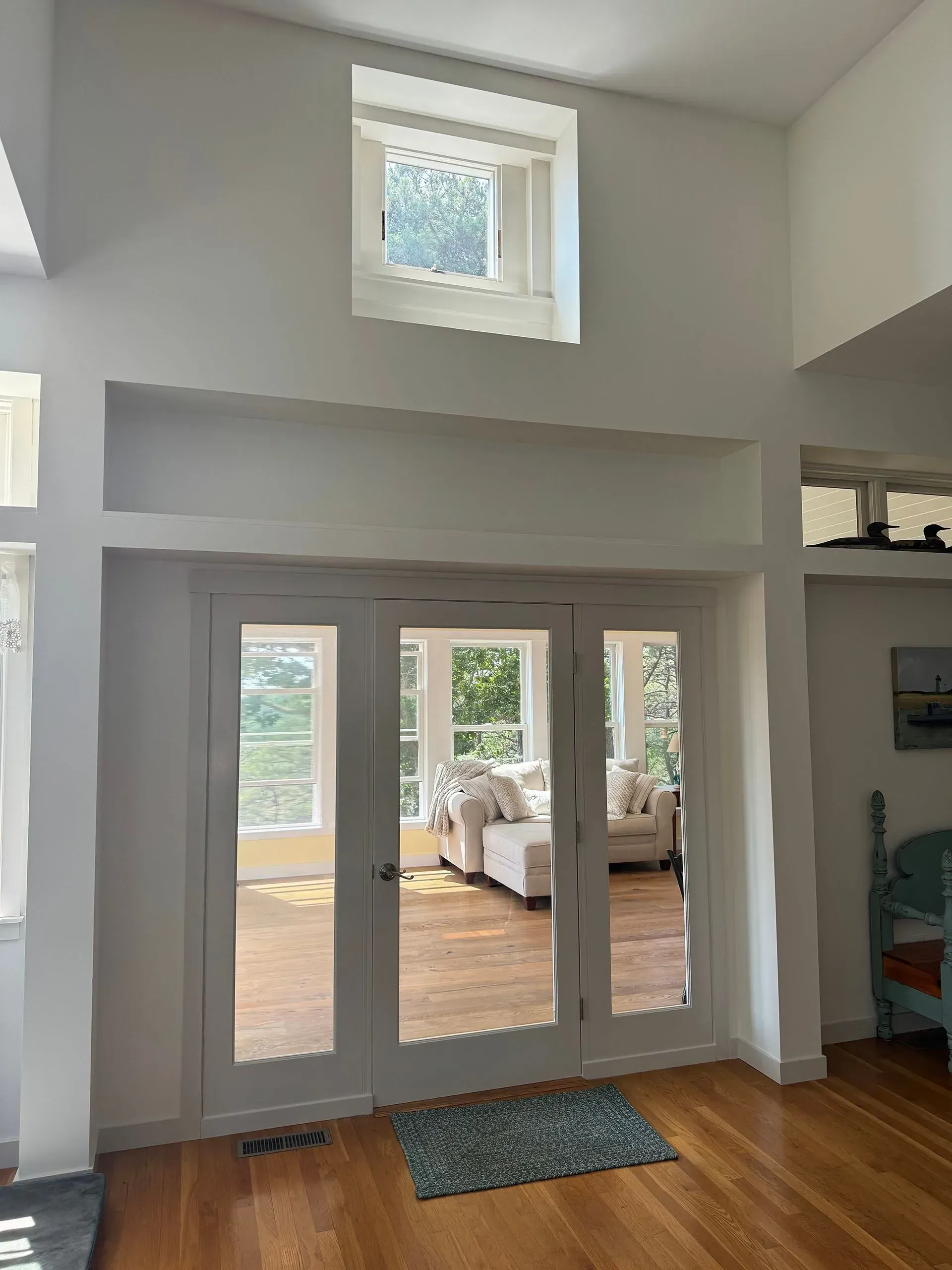 Interior view with French doors, built-in shelving, and a high window.  White walls and hardwood floors.