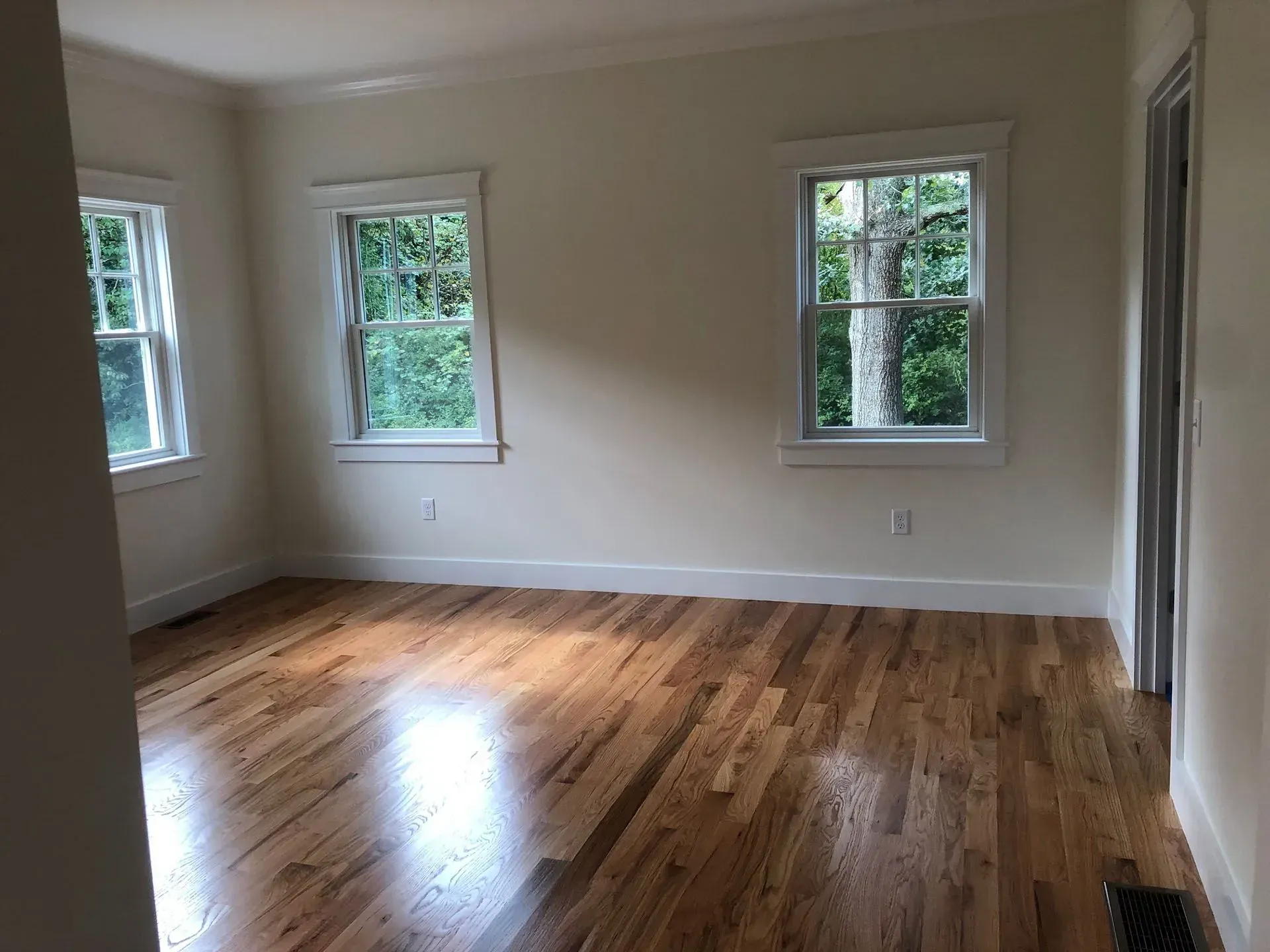 Empty room with hardwood floors, three windows, and white walls.