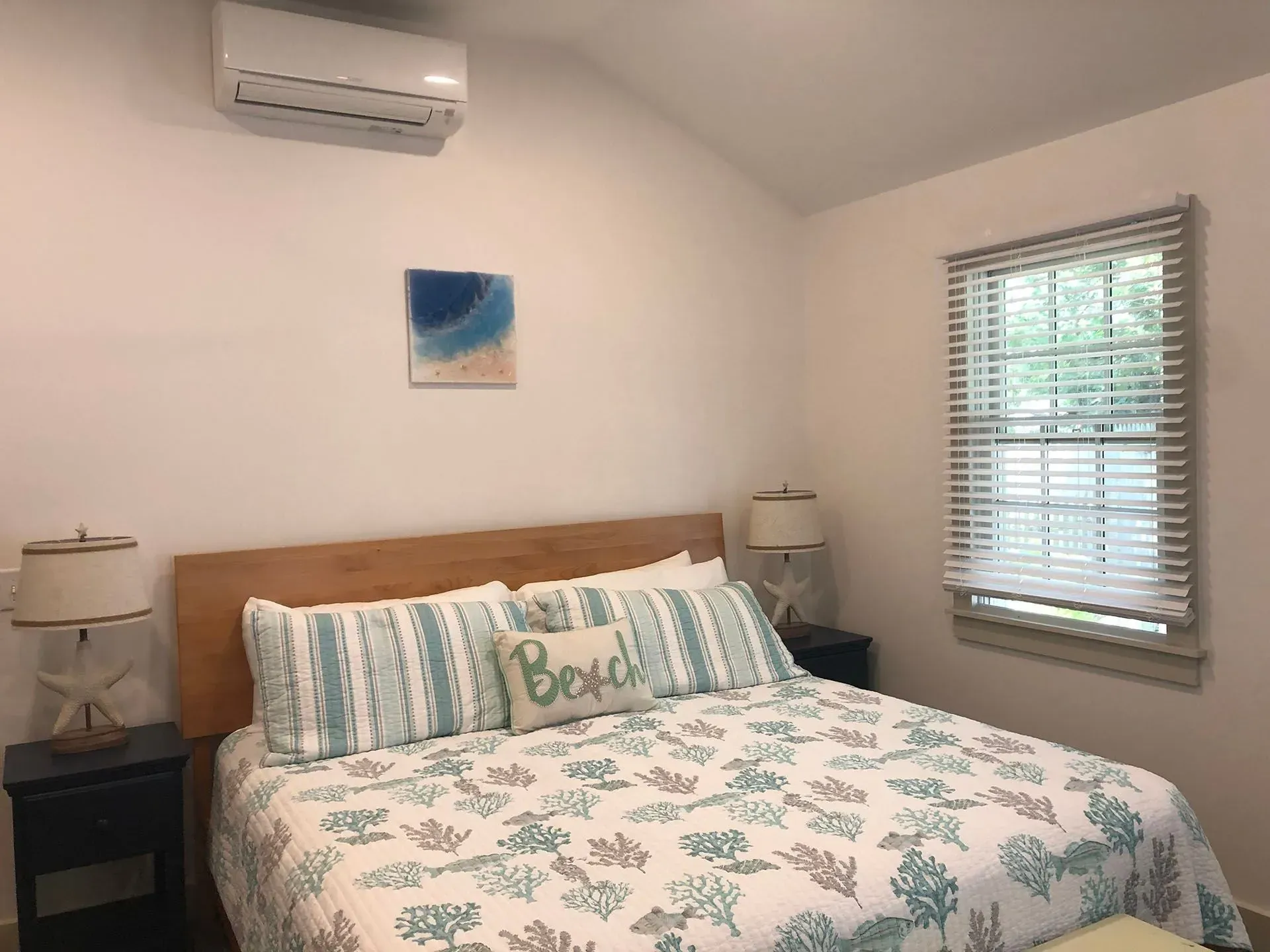 Bedroom with bed, nightstands, window with blinds, and AC unit. Coastal decor.
