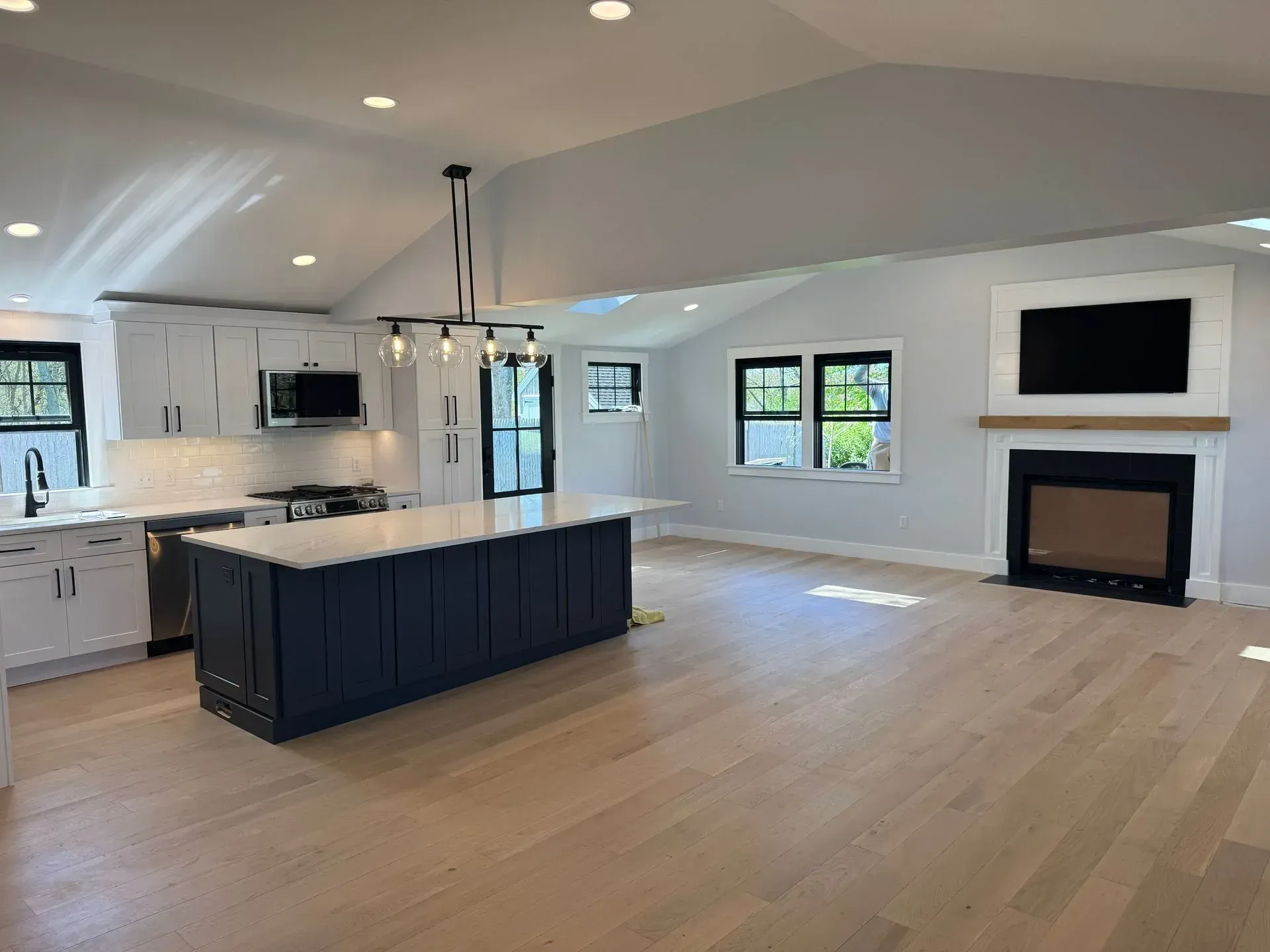 Modern kitchen and living space with white cabinets, blue island, fireplace, and light wood floors.