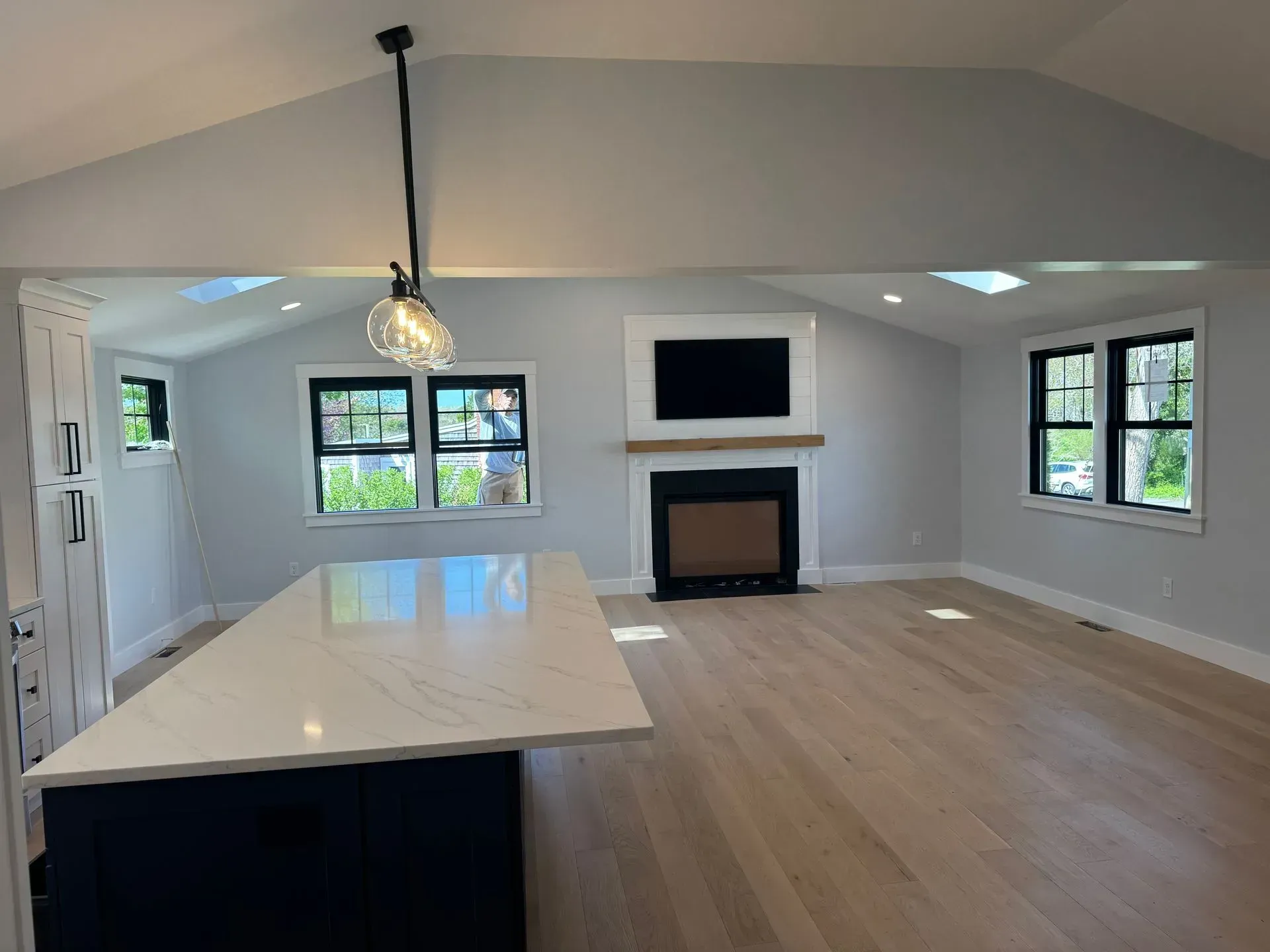 Modern kitchen and living area with a dark blue island, white countertops, and light gray walls. Fireplace and light wood floors.