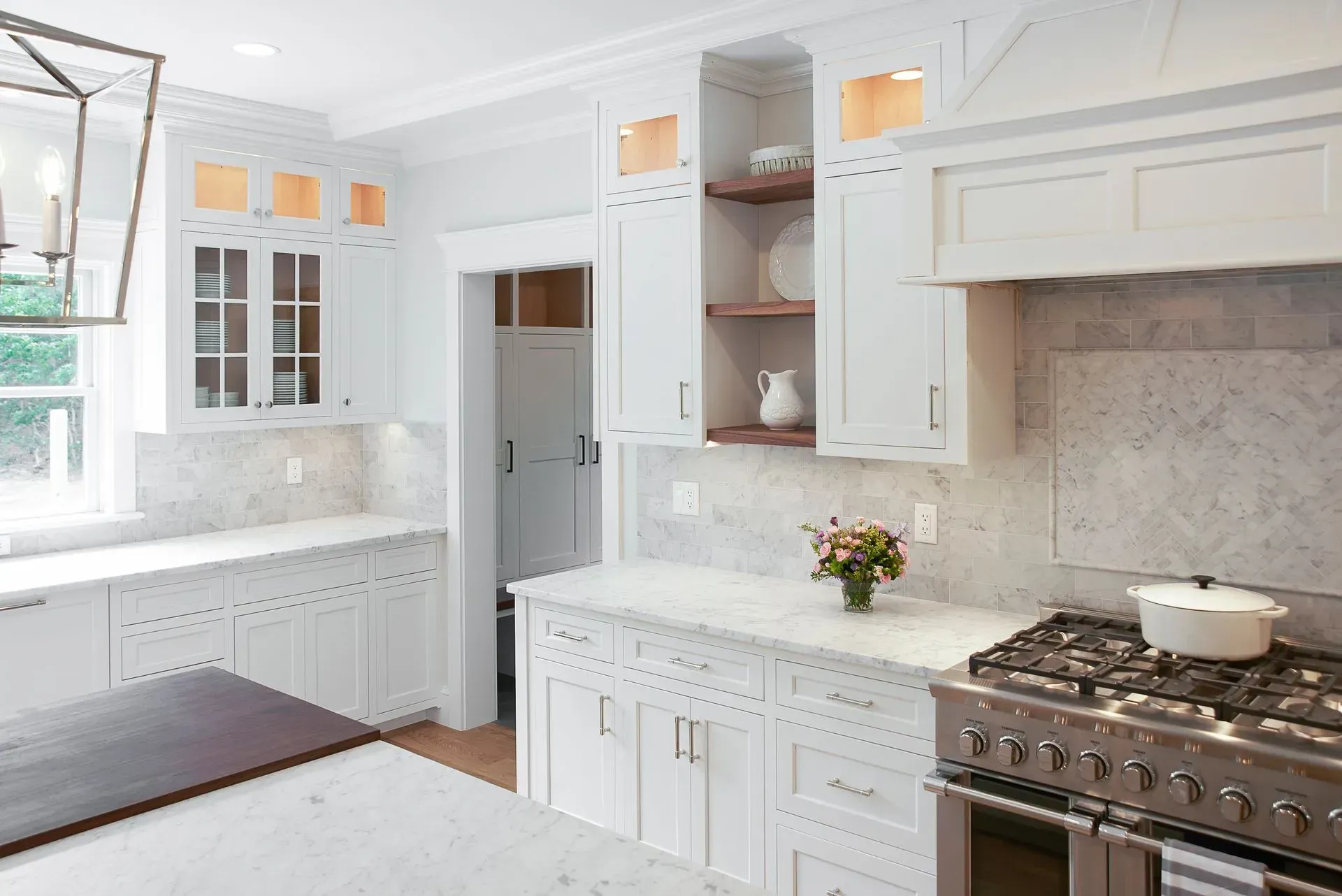 White kitchen with marble countertops, stainless steel stove, and white cabinets.