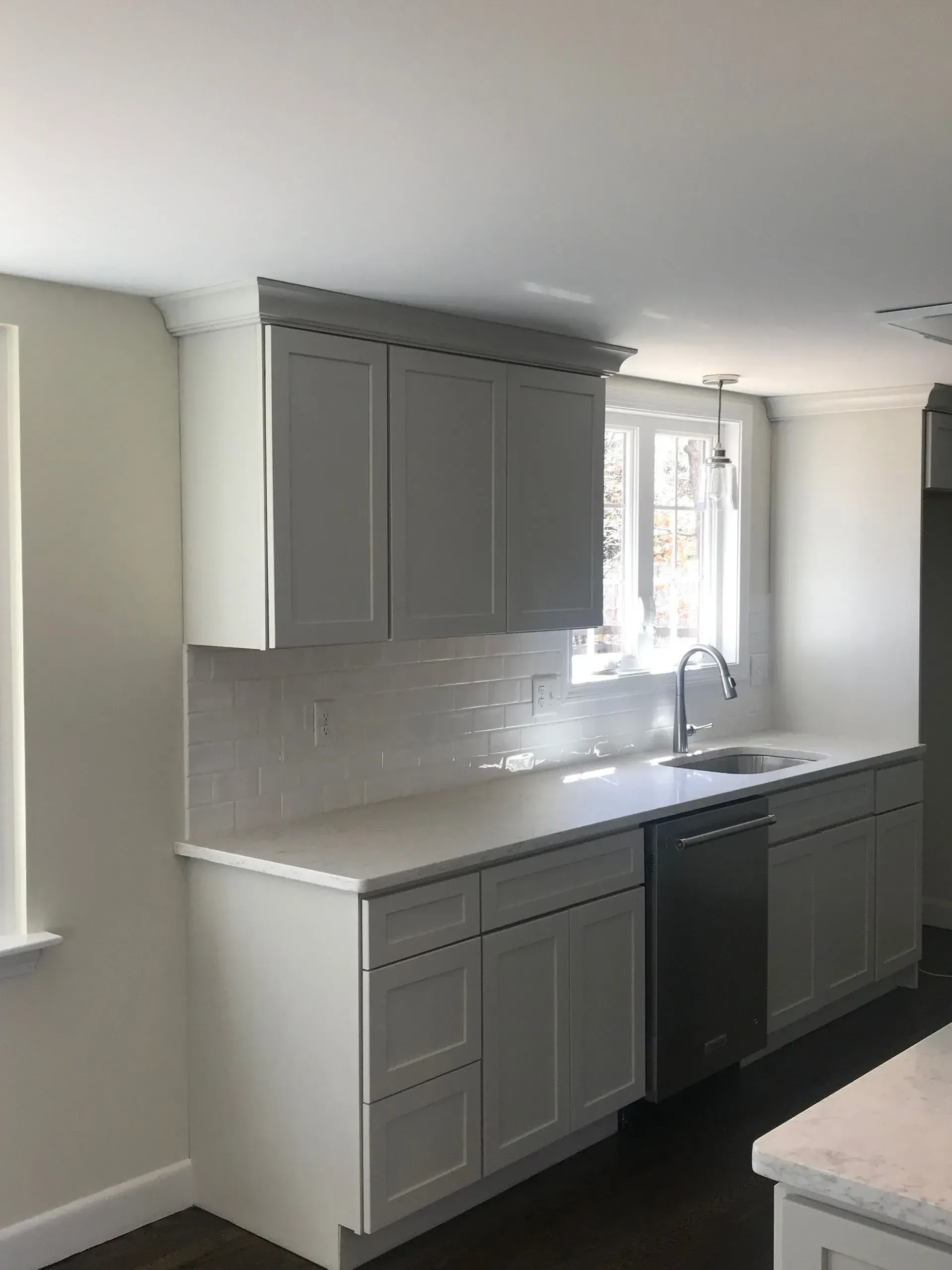 White kitchen cabinets with white countertops and a stainless steel sink and dishwasher.