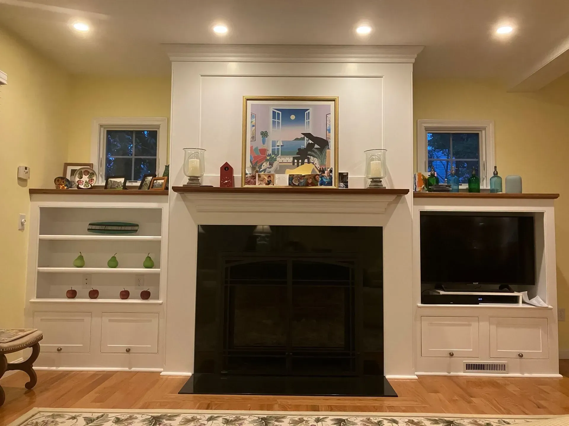 Fireplace with built-in bookshelves and a TV, all white, with a black fireplace front and dark wood mantel.