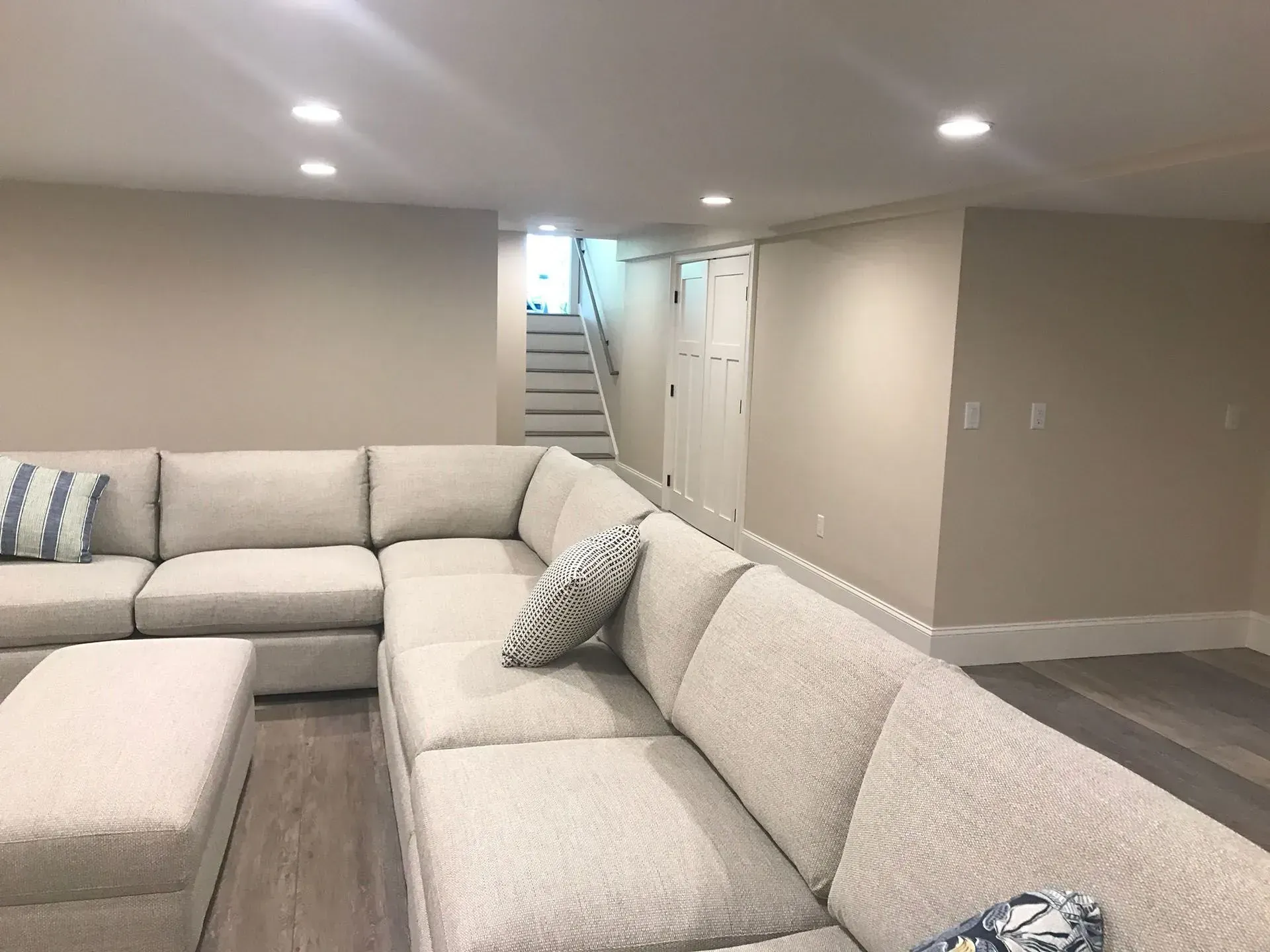 Beige sectional sofa in a finished basement with stairs and doors.