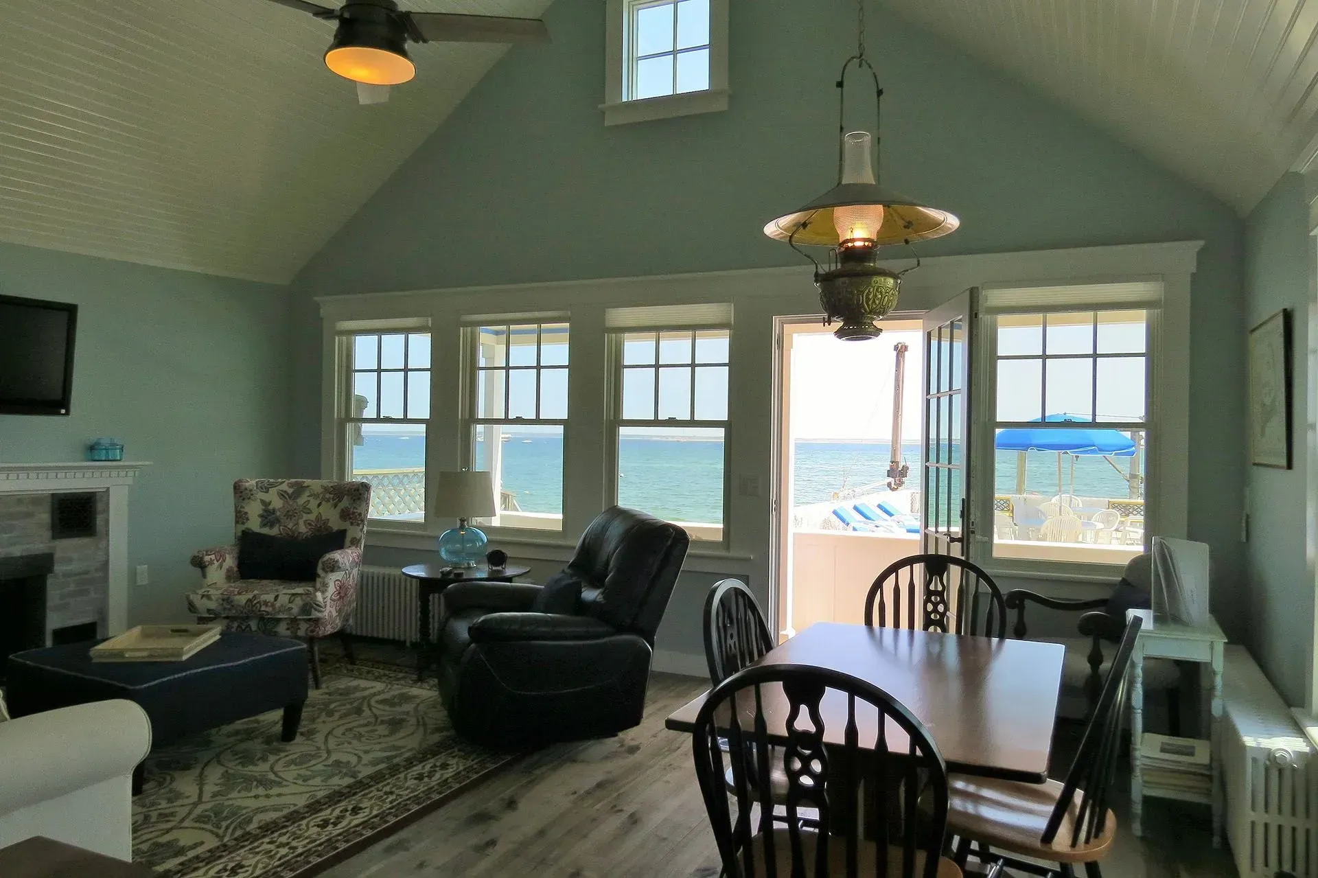 Living room with ocean view, pale blue walls, multiple windows, dining table, and cozy seating.