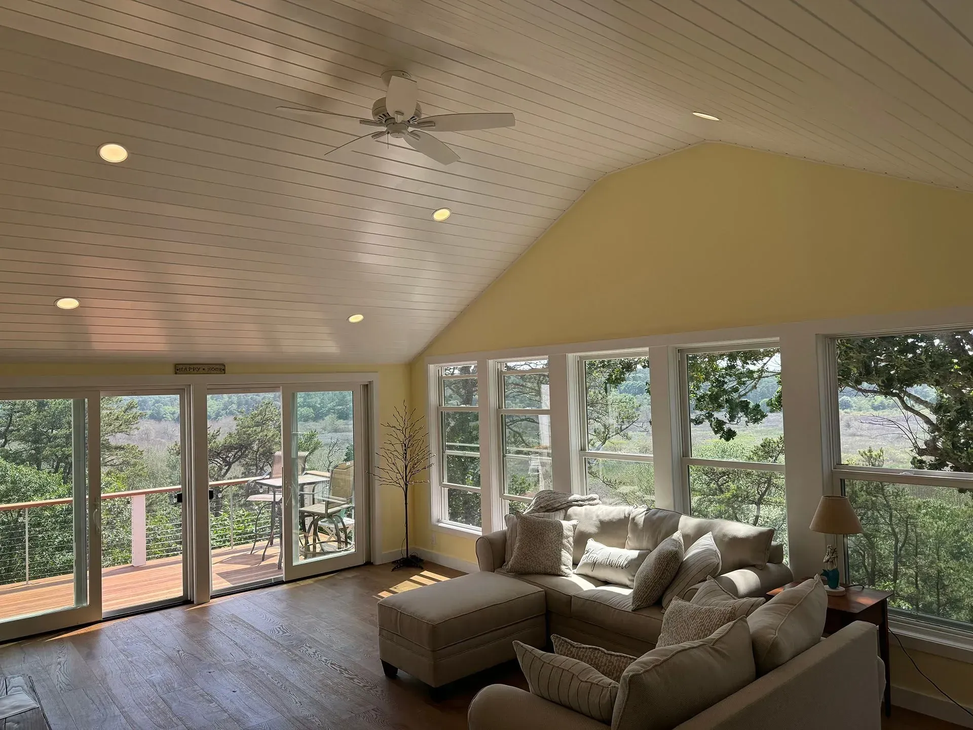 Living room with vaulted ceiling, large windows, and a sectional sofa overlooking a wooded view.