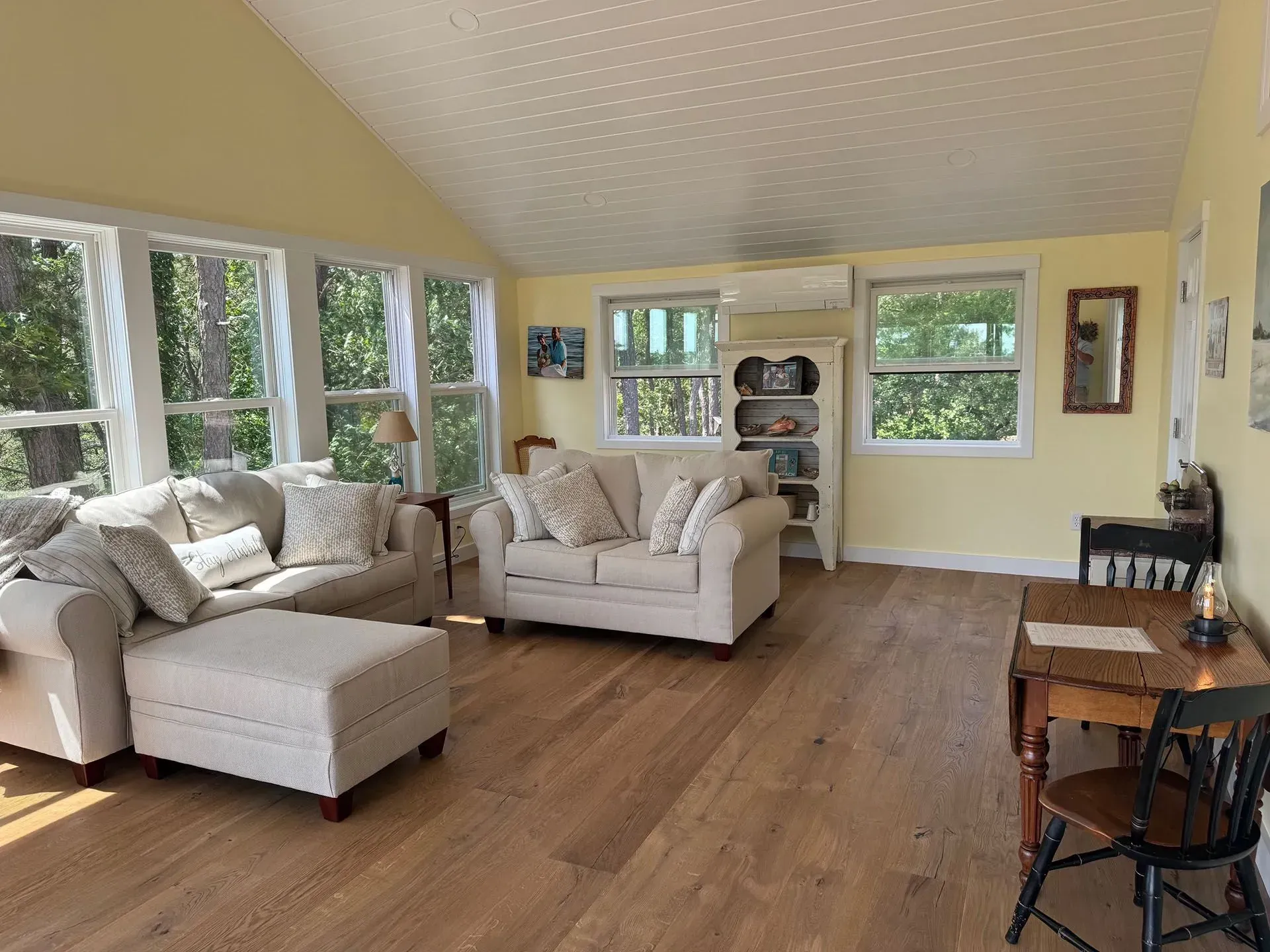 Bright, sunny living room with hardwood floors, two beige sofas, and numerous windows.