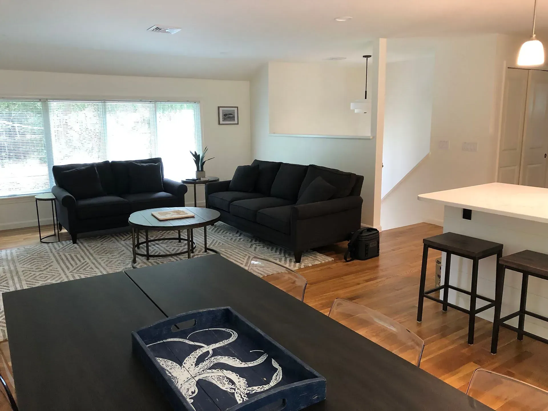 Living room with dark couches, a coffee table, and a kitchen island with stools.