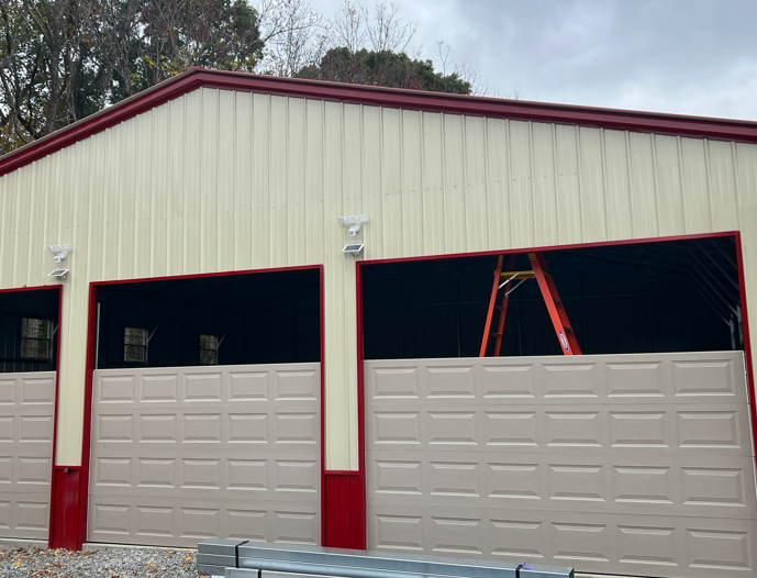 Beige metal garage with red trim, two open roll-up doors, and an orange ladder inside, set against a cloudy sky.