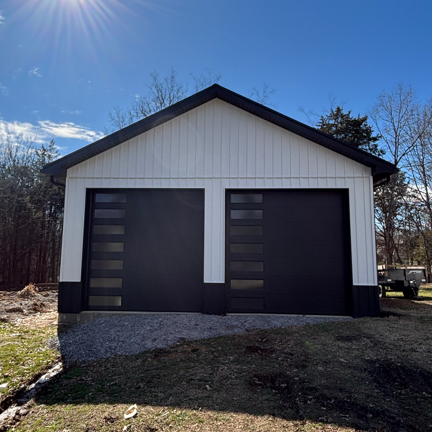 A white and black detached garage with two modern garage doors featuring vertical glass panels under a bright blue sky.