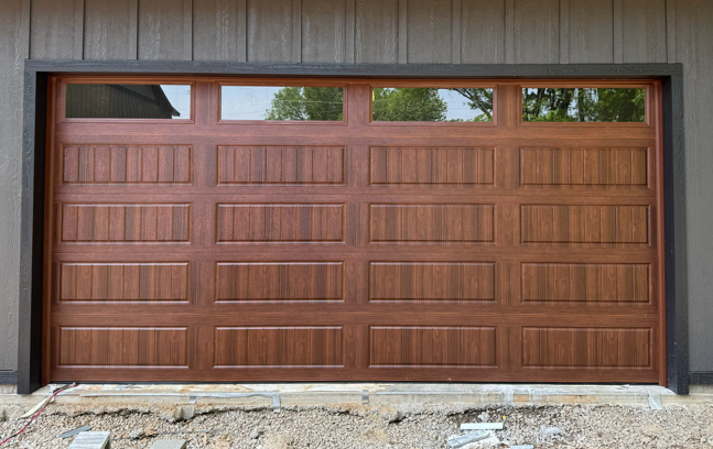 A modern, wood-look sectional garage door with a four-panel horizontal design and a top row of windows.