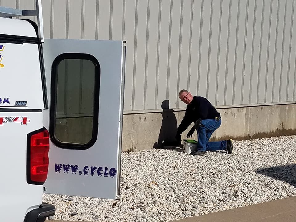 A man is kneeling in front of a white truck with a sign that says www.cyclo on it.