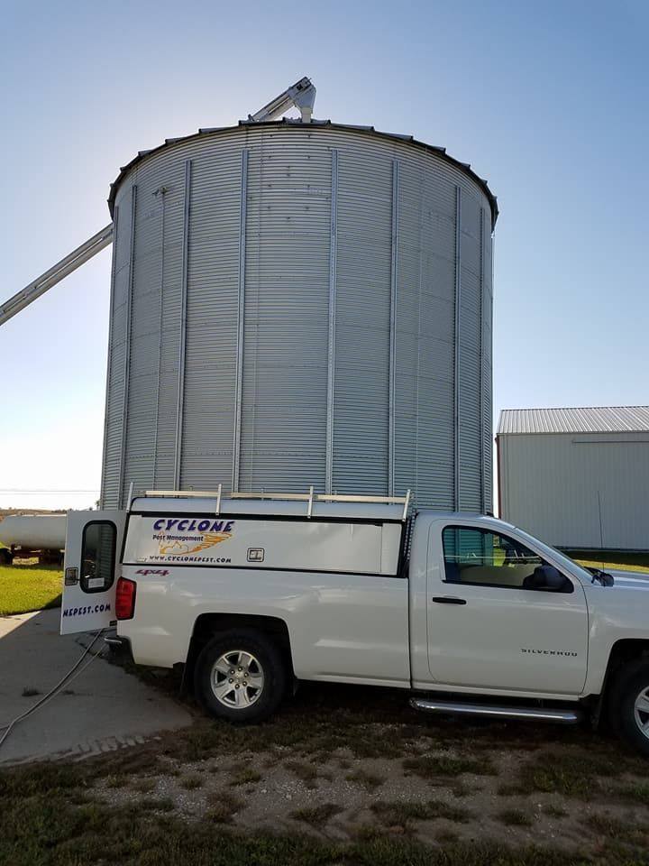 A white truck is parked in front of a large silo.