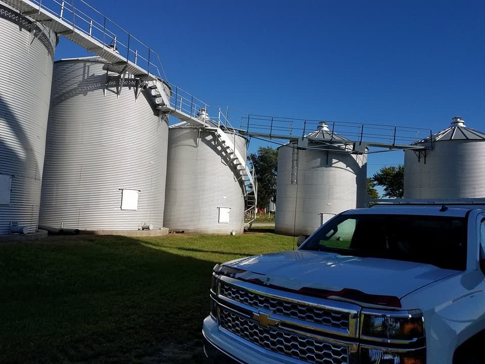 A white truck is parked in front of a row of silos