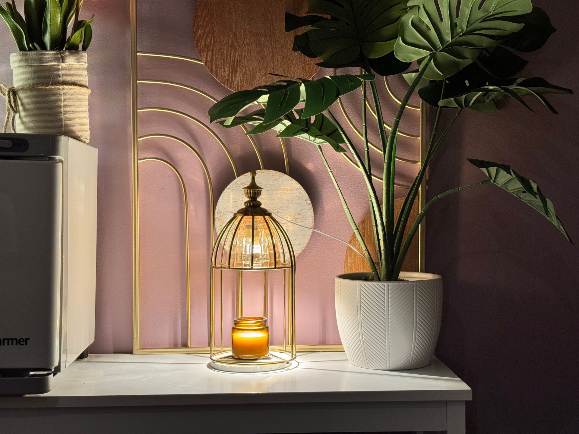 White table with gold and pink decor, including a lit candle lantern and potted plants.