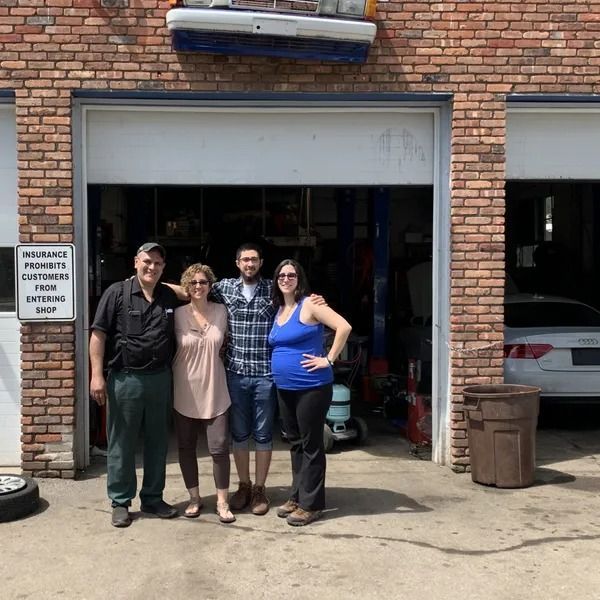 Four people stand in front of a garage door. The setting is a brick building, and the individuals are smiling.