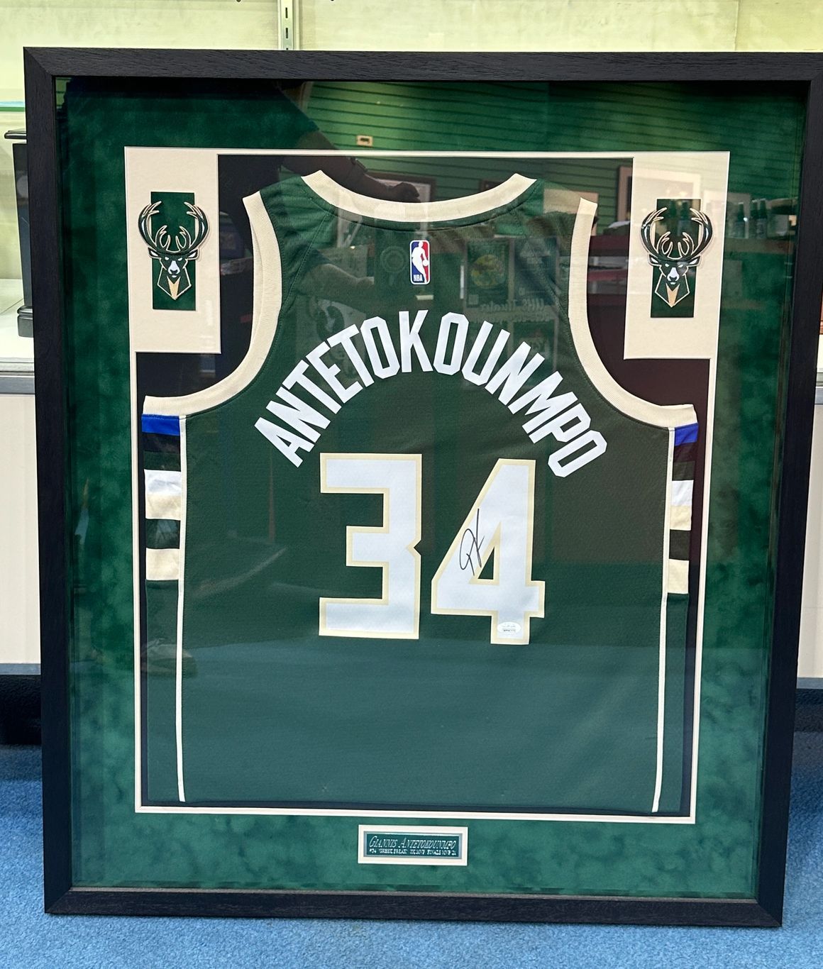 Framed Milwaukee Bucks jersey of Antetokounmpo, number 34, in a green and white design, signed, displayed against a green background.