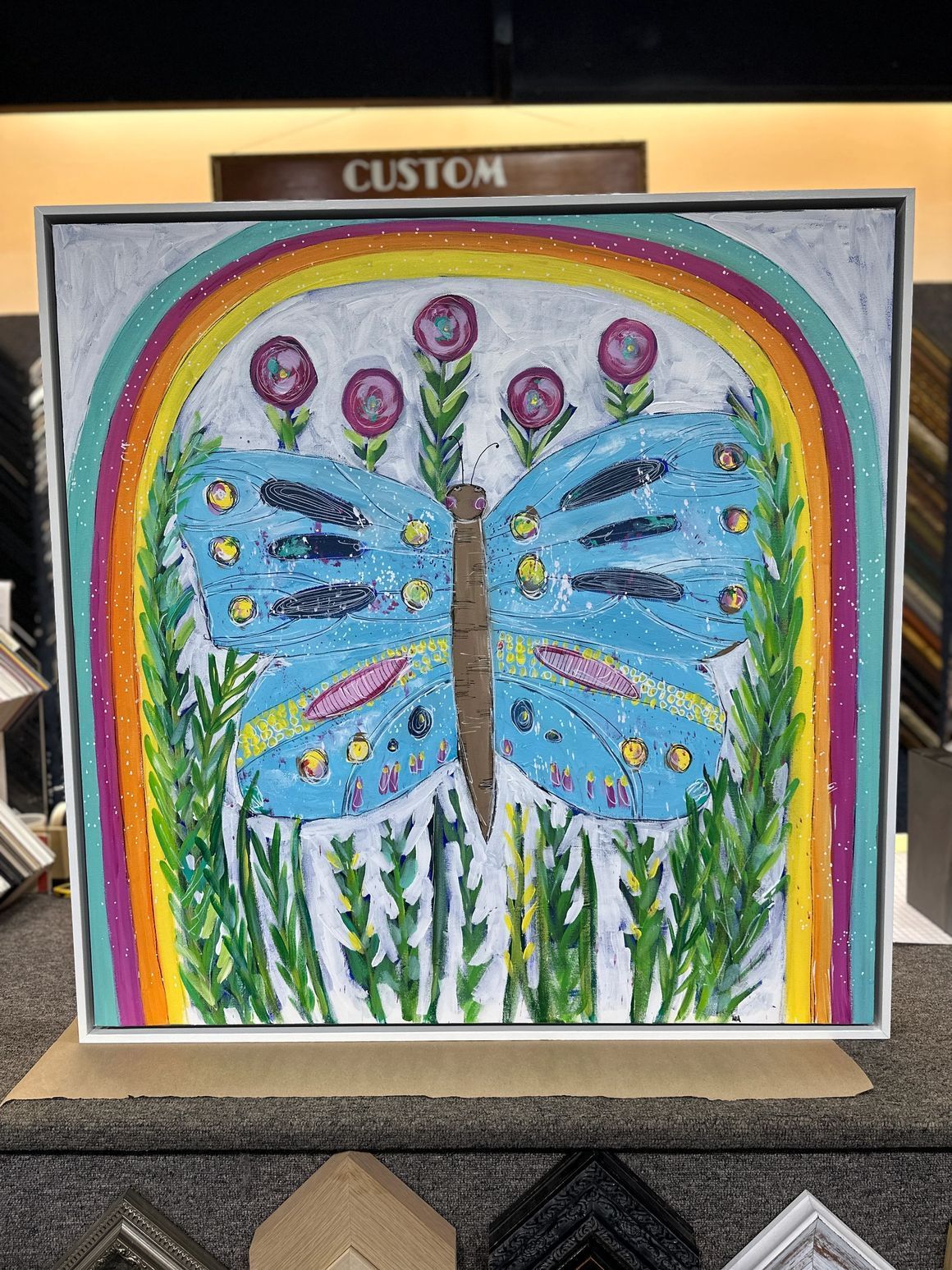 Colorful butterfly painting framed with a rainbow, flowers, and green grass.