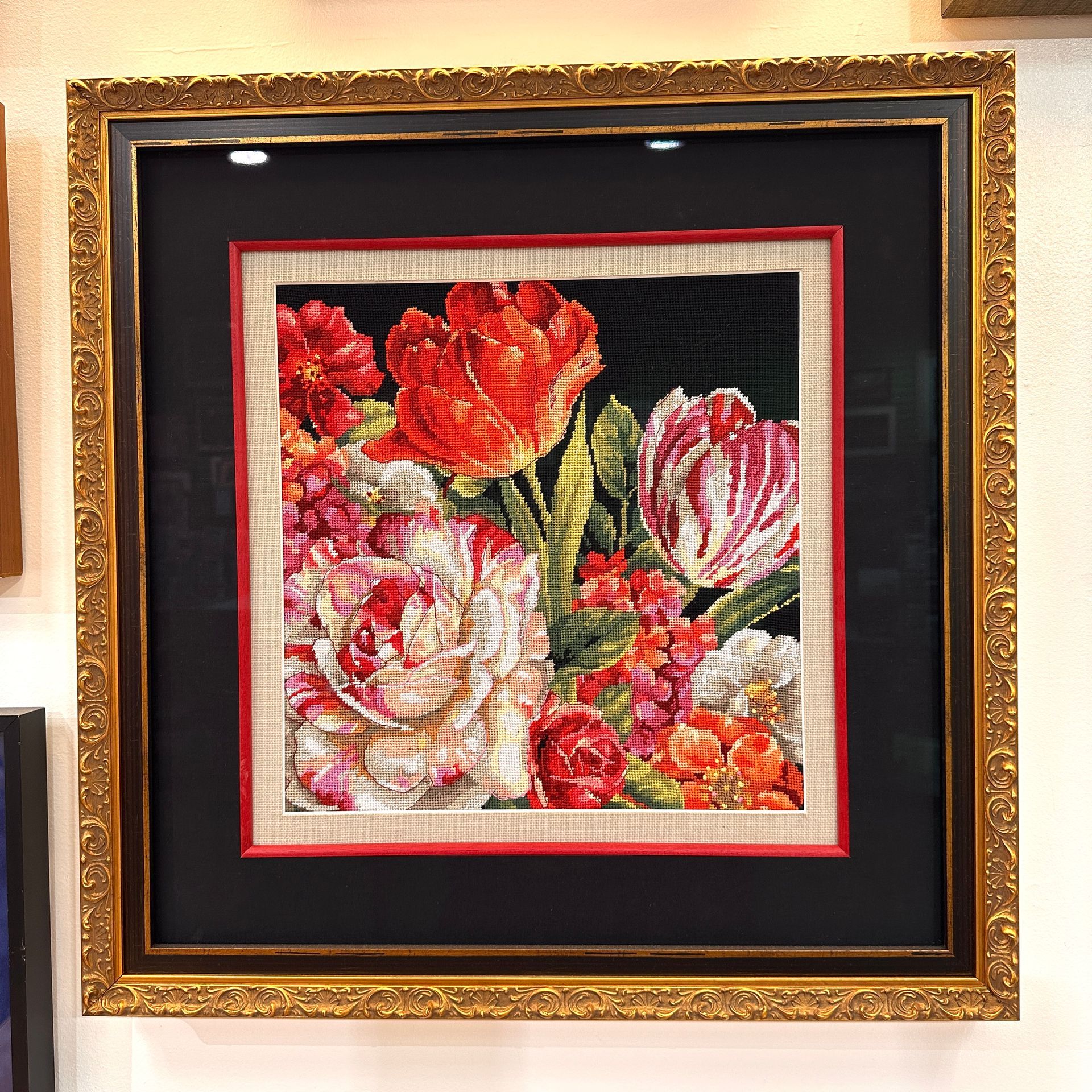 Framed needlepoint of colorful flowers, red, pink, white, and orange, on a black background.