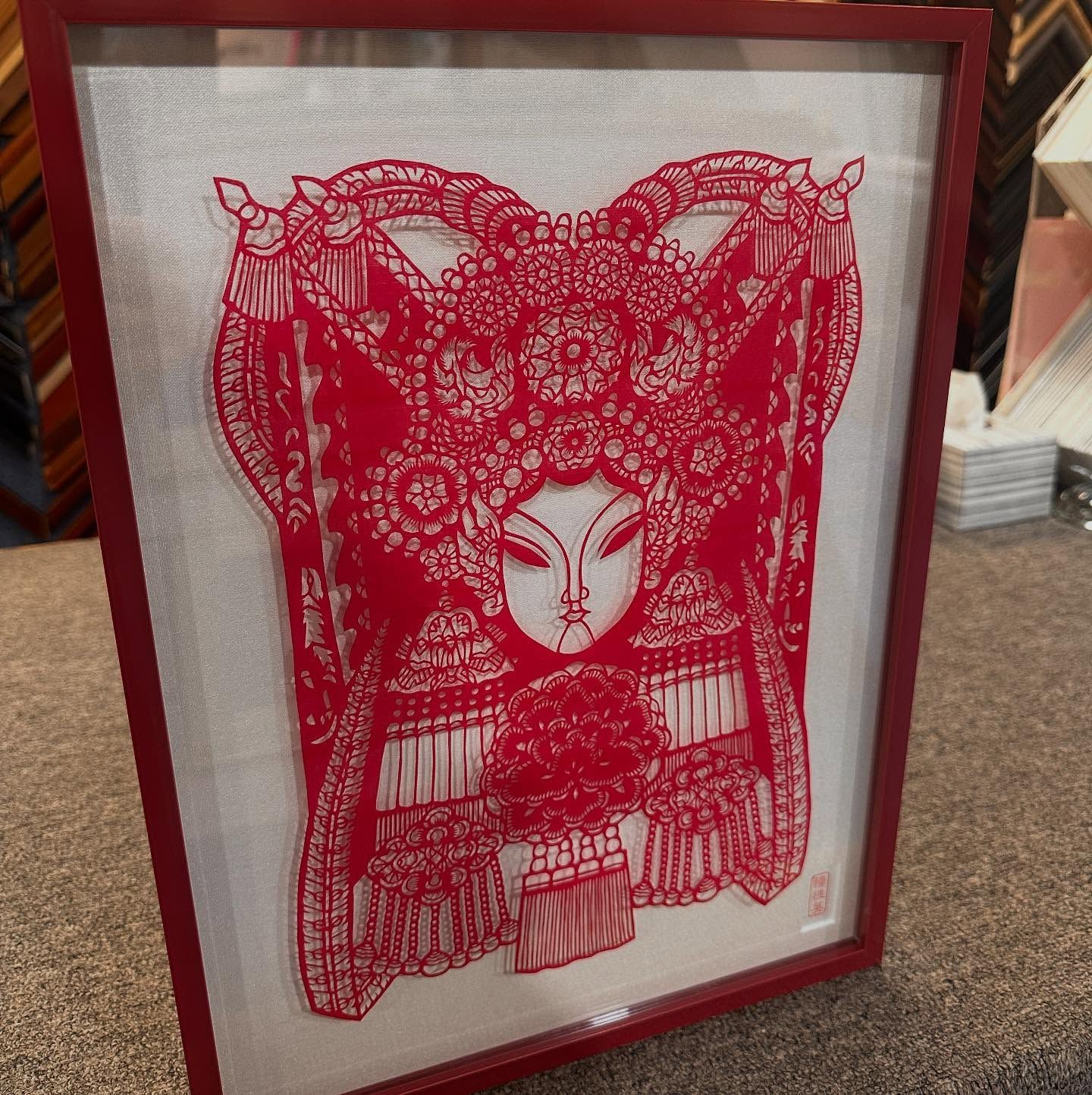 Red paper cut art of a woman in a headdress, framed in a red frame, against a white backdrop.