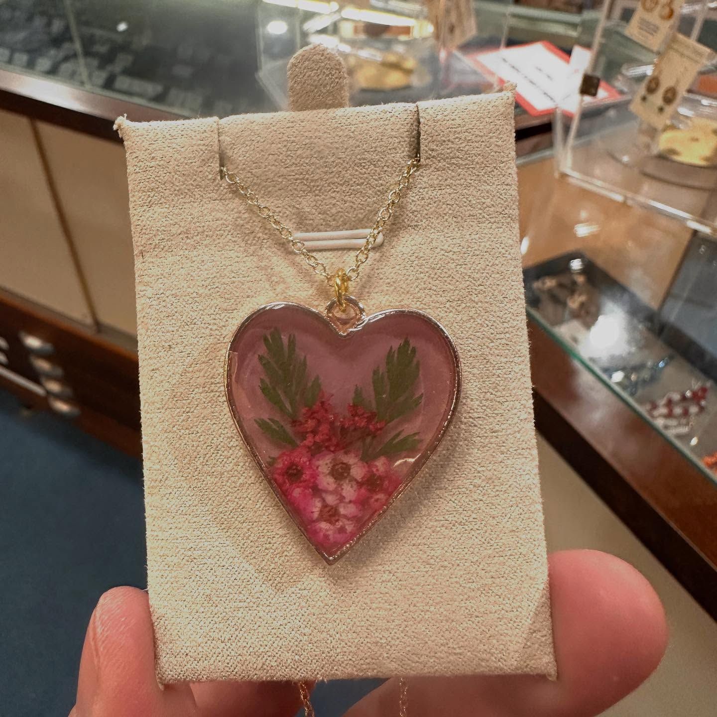 Heart-shaped pendant necklace with pink flowers encased in clear resin, held by a person.