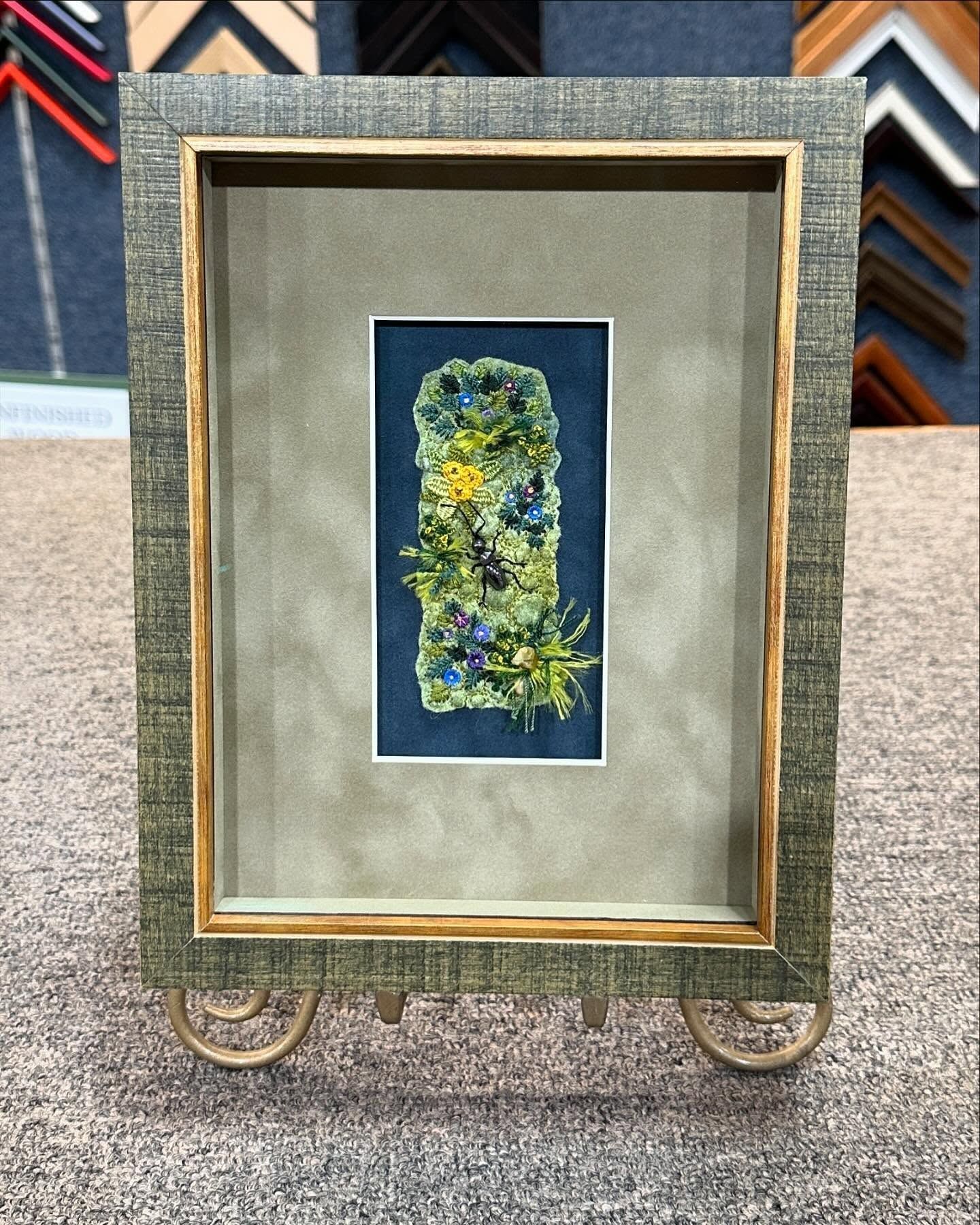 Framed floral art in a gray and gold decorative frame, displayed on a stand.