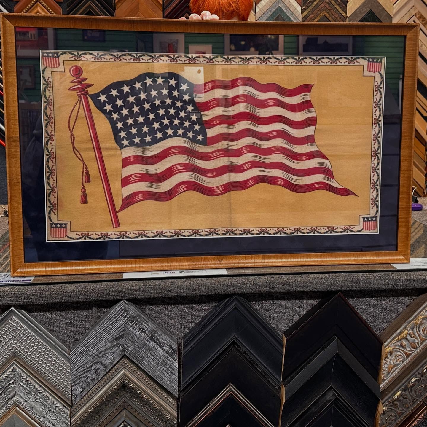 American flag art in a gold frame, displayed above framing samples.