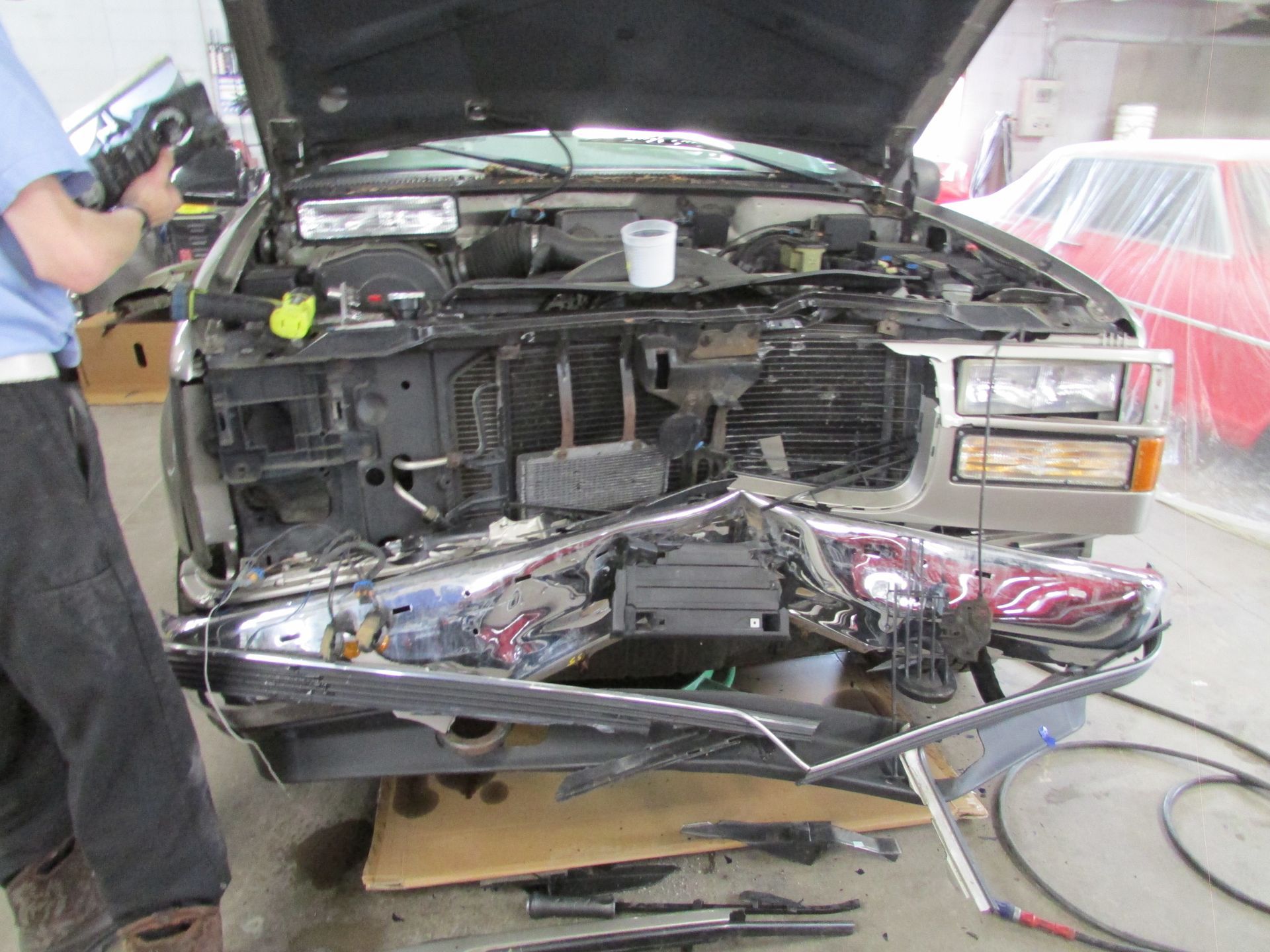Truck with damaged front end in a garage, a person in blue shirt works on it.