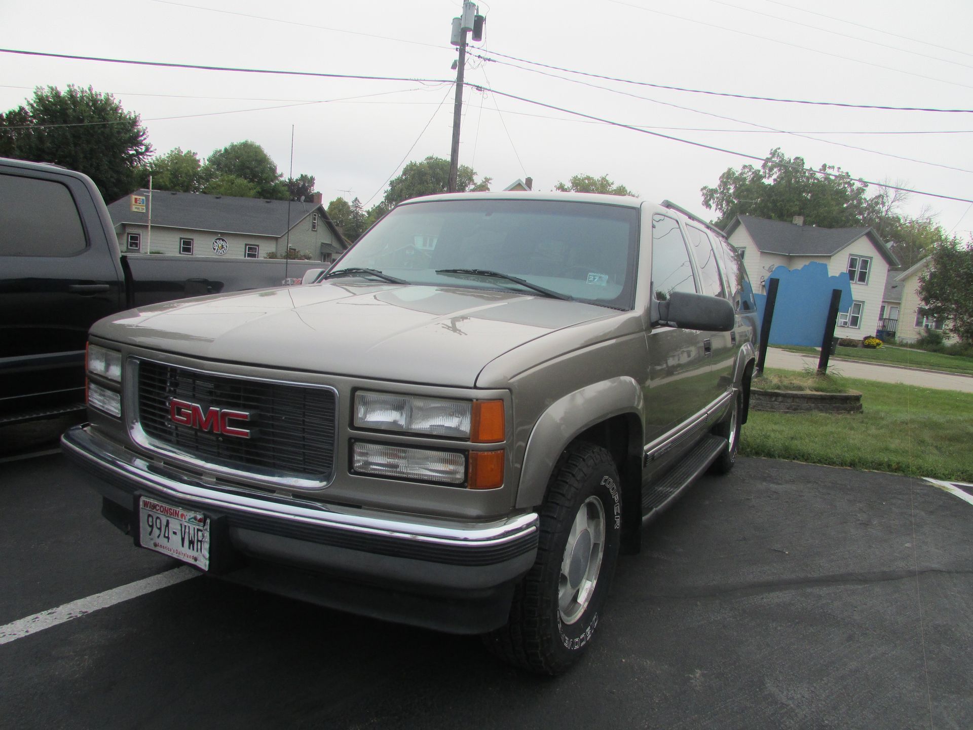Tan GMC Yukon SUV parked on asphalt, cloudy day.