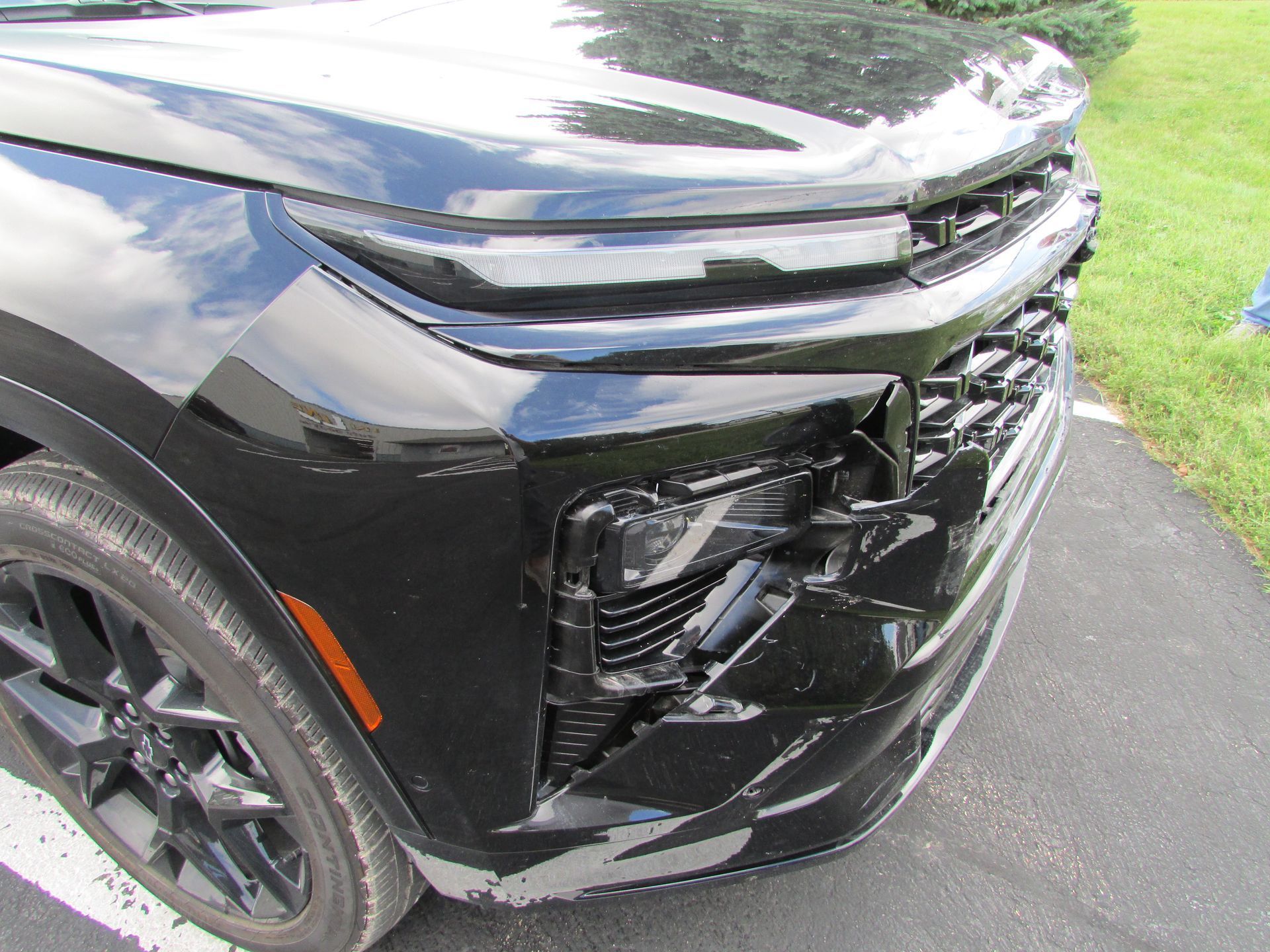 Damaged black SUV front bumper and headlight. Close-up, outdoor setting.