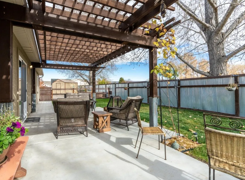 Patio with pergola, wicker furniture, and yard, with fence.
