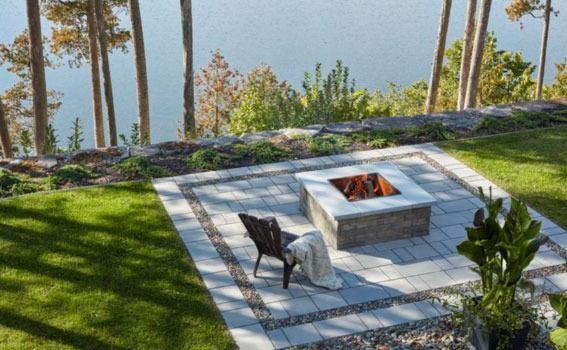 Stone patio fire pit with two lounge chairs overlooking a grassy hillside and trees