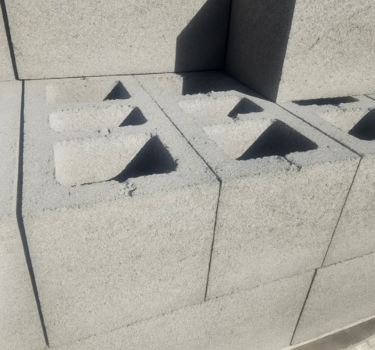 Gray concrete blocks with triangular cutouts stacked in a sunlit outdoor setting