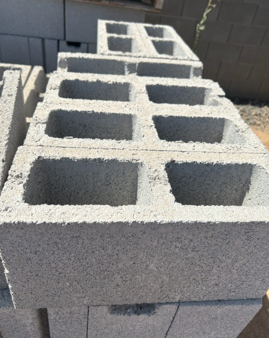 Stacked gray concrete cinder blocks outdoors in front of a dark wall.