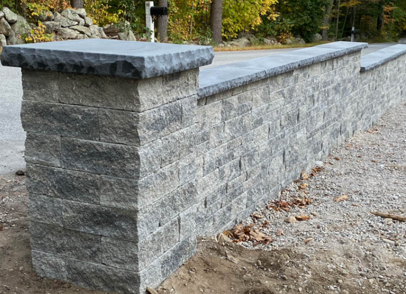 Gray stone retaining wall with a dark cap along a gravel path