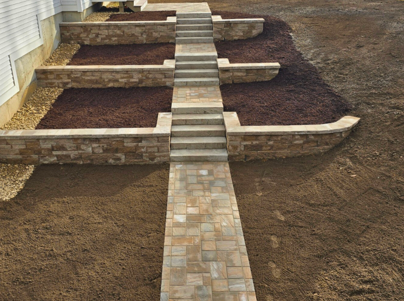 Raised garden beds with a stone walkway in the center of a landscaped yard.