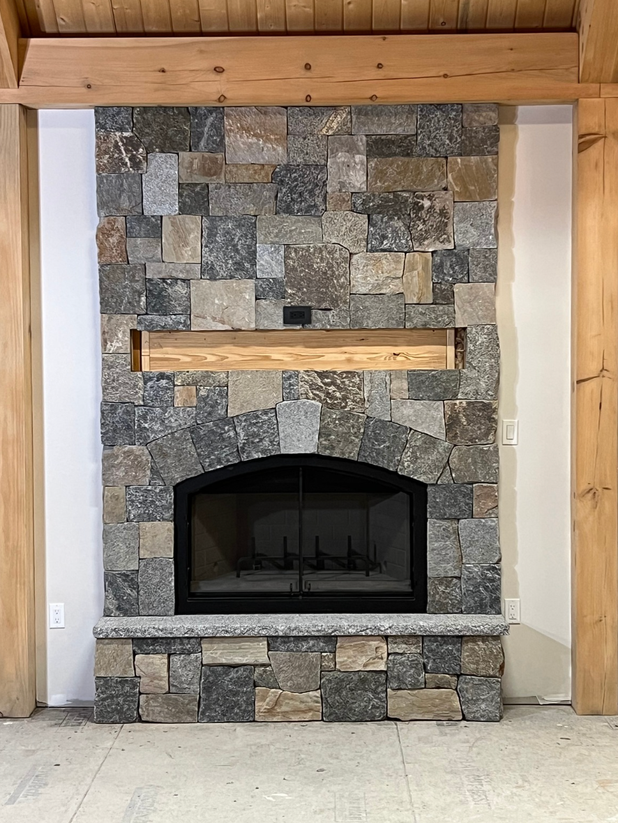 Stone fireplace with wood mantel and arched black firebox in a rustic room.