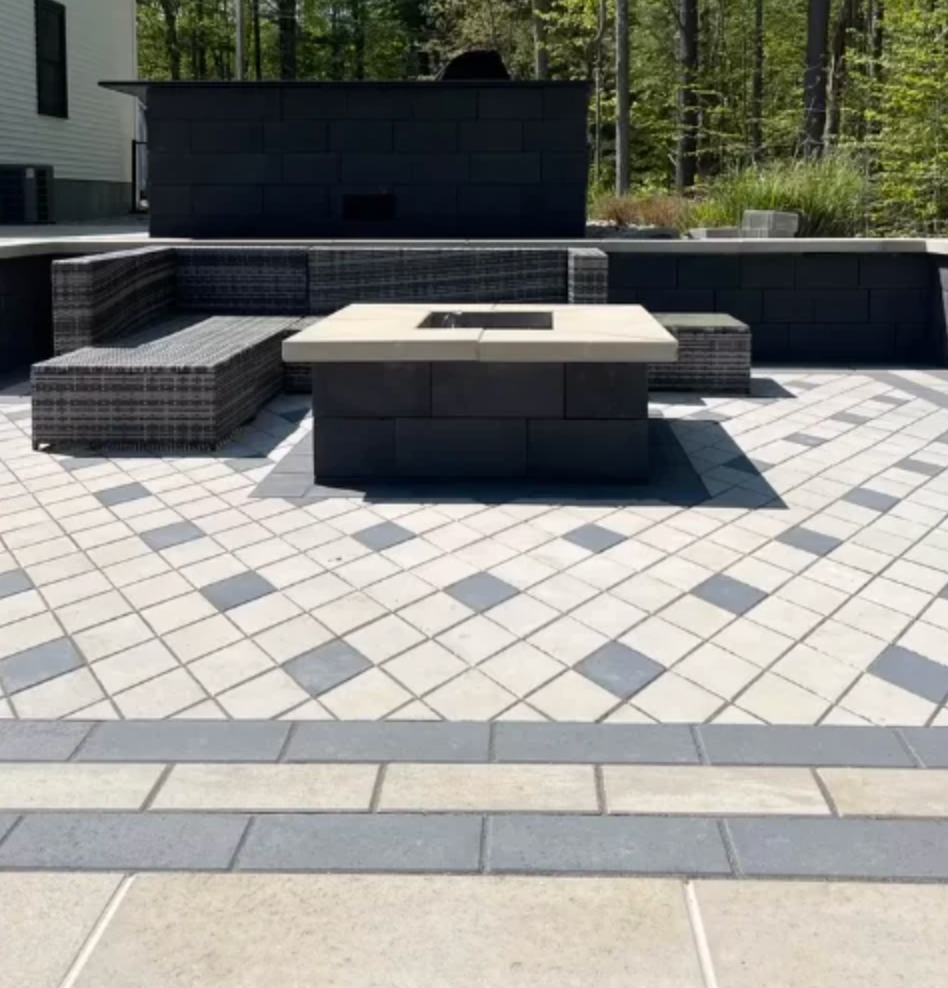 Modern patio with gray pavers, built-in dark seating, and a central concrete fire pit table under trees.