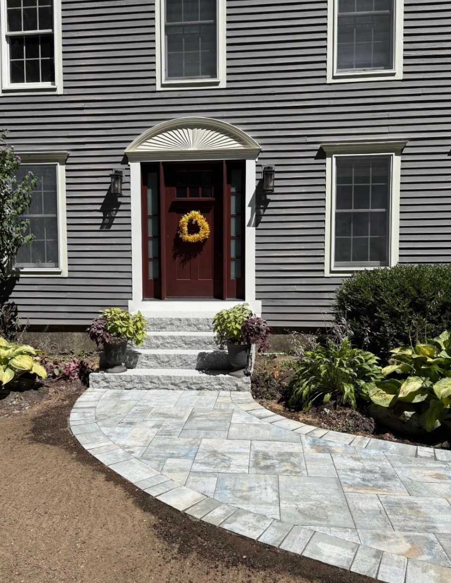Front of gray house with stone walkway, white steps, and red front door with a wreath.