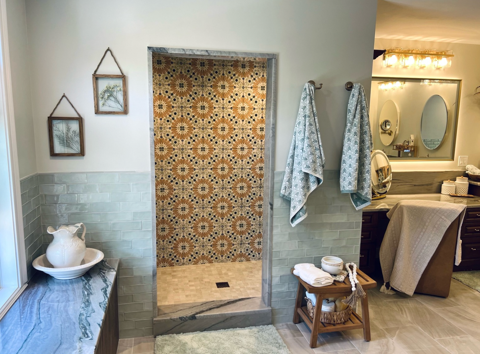 Spa-like bathroom with patterned shower curtain, blue tile sink, towels, and vanity mirror lights.