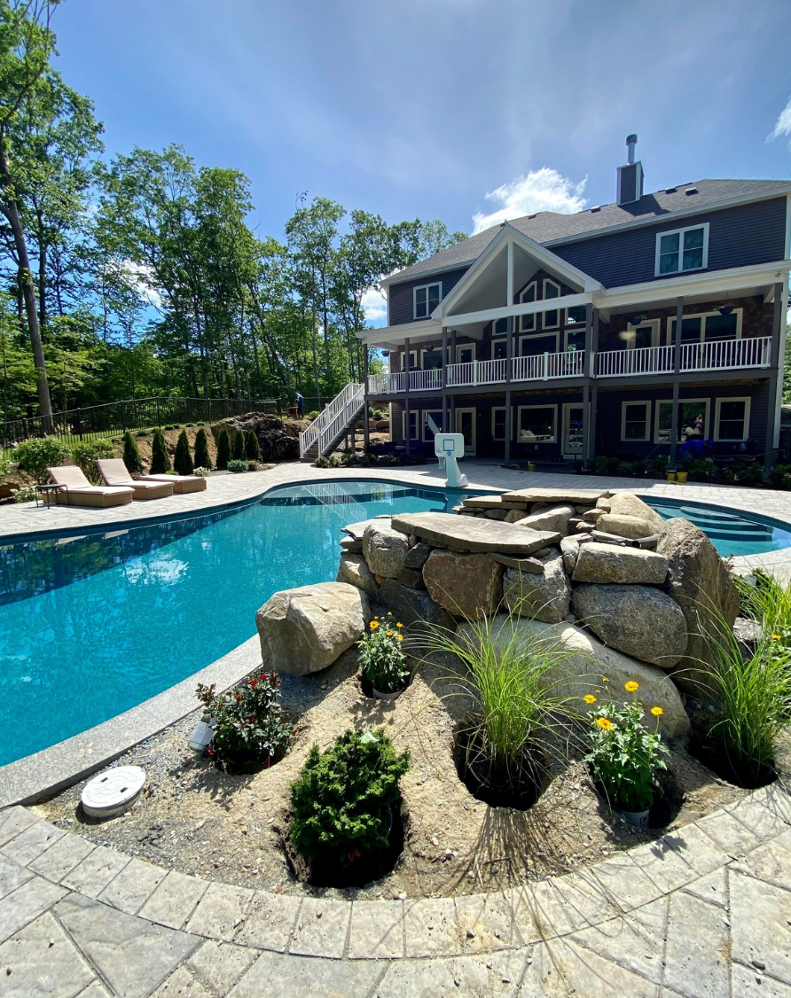 Luxury house with backyard pool, stone landscaping, and blue sky.