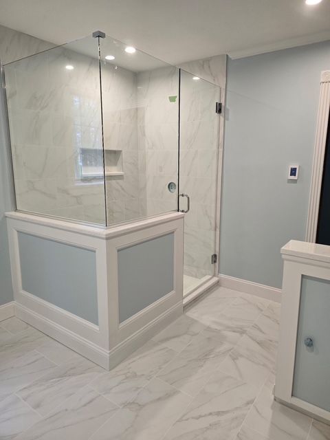 Glass-enclosed marble shower with a built-in shelf and chrome fixtures in a bright bathroom.