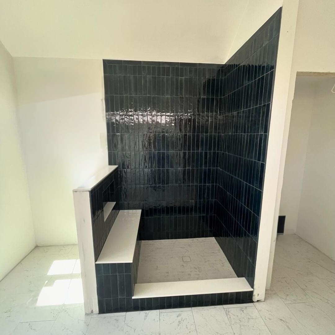 Tiled walk-in shower with black wall tiles, white seat, and light floor in a bathroom.