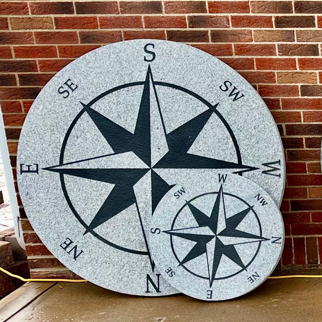 Stone compass rose plaque with black star and direction labels leaning against a brick wall.