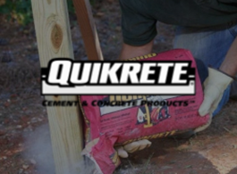 Person holding a pink Quikrete concrete mix bag outdoors near wooden posts