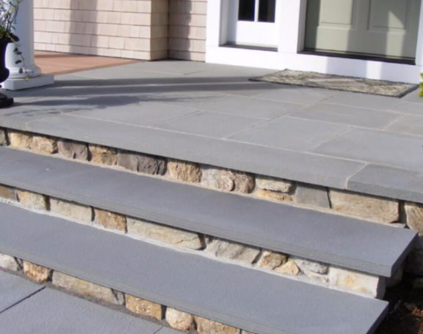 Front steps of a house with gray stone treads and beige stone risers leading to a white door.