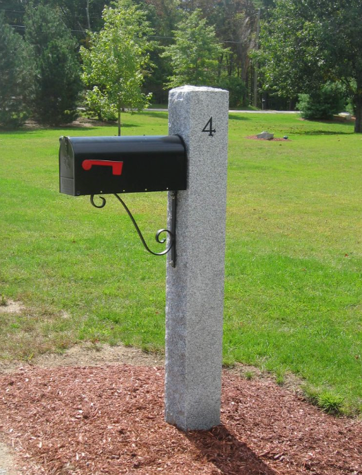 Black mailbox on a gray post labeled 4 in a grassy yard with trees behind it