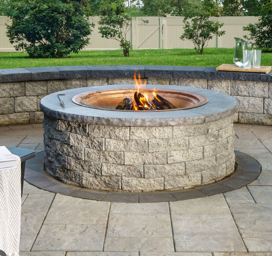Stone fire pit with a small flame in a landscaped outdoor patio area